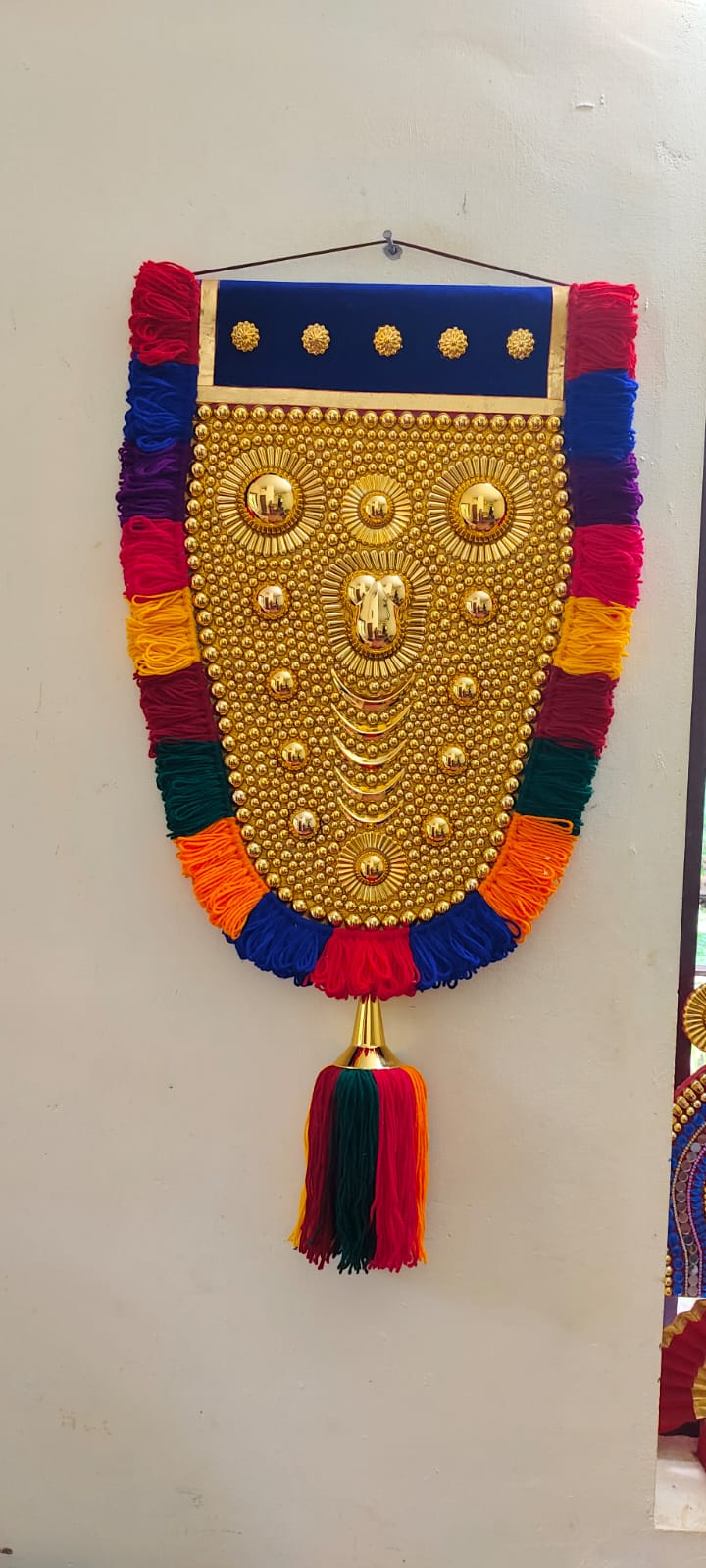 Decorative wall hanging with colorful tassels and gold embellishments on a white background