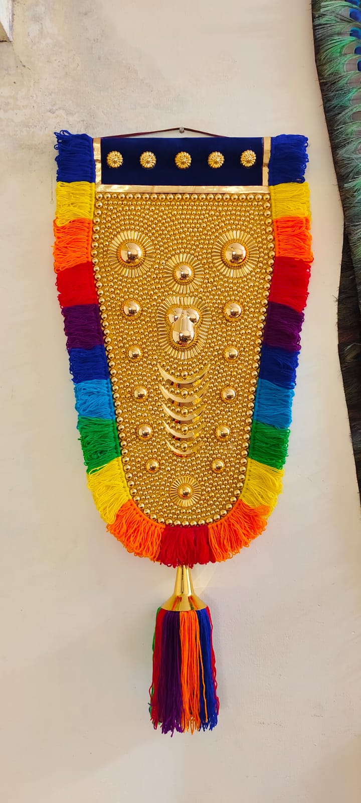 Decorative wall hanging with gold center, rainbow fringes, and tassels on a light background